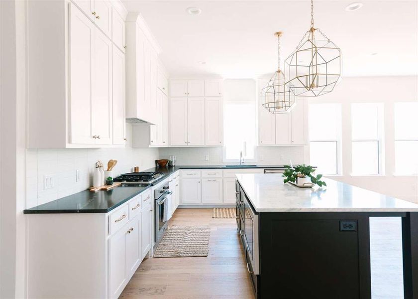 Kitchen with white cabinets, a kitchen island, decorative light fixtures, appliances with stainless steel finishes, and light hardwood / wood-style floors