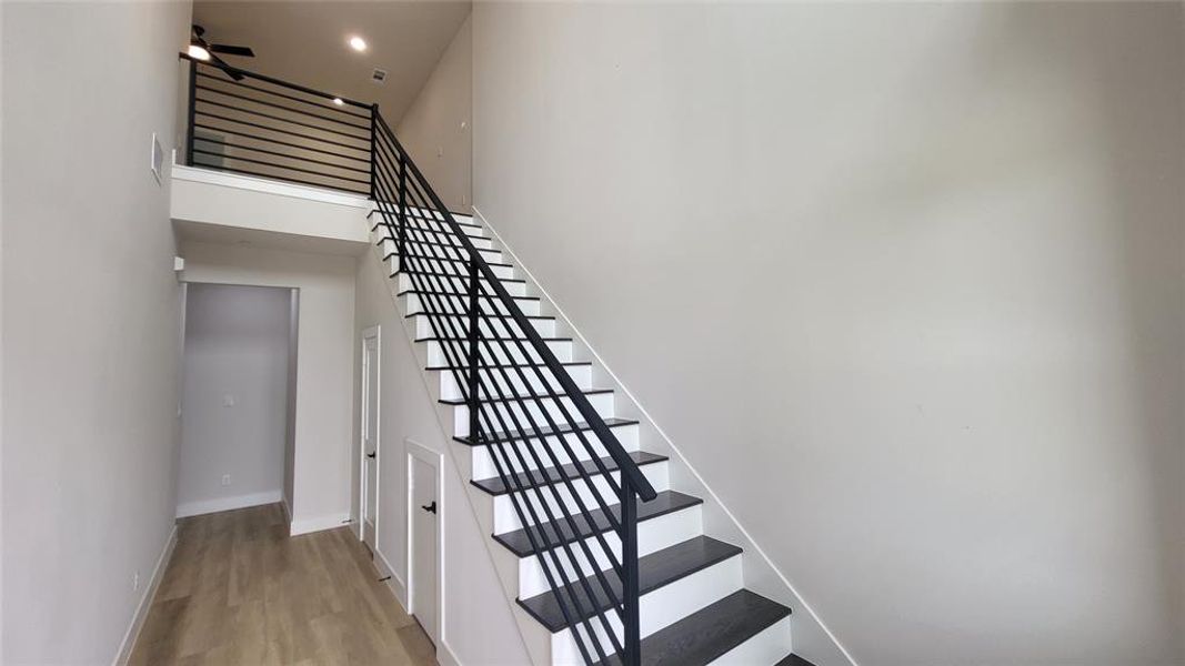 Stairs featuring wood finished floors, a high ceiling, a ceiling fan, and baseboards