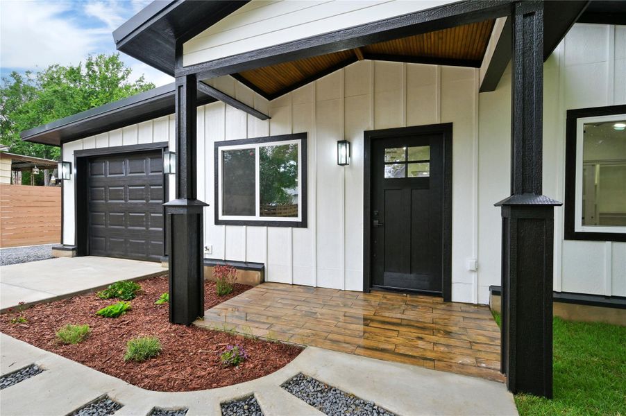 Doorway to property with board and batten siding, a garage, and driveway