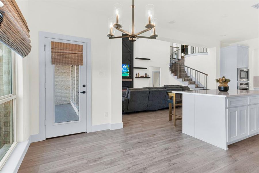 Kitchen with light stone counters, light wood finished floors, pendant lighting, open floor plan, and a chandelier Kitchen with light stone counters, light wood finished floors, pendant lighting, open floor plan, and a chandelier