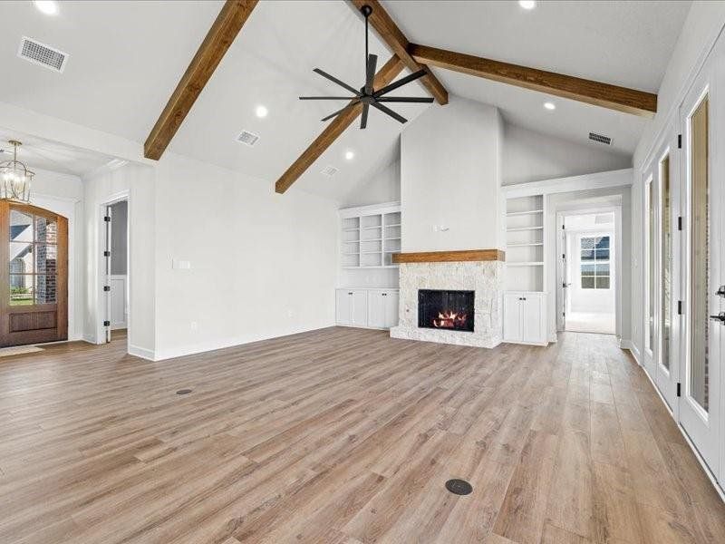 Unfurnished living room with a stone fireplace, recessed lighting, built in features, light wood-type flooring, and beam ceiling Unfurnished living room with a stone fireplace, recessed lighting, built in features, light wood-type flooring, and beam ceiling