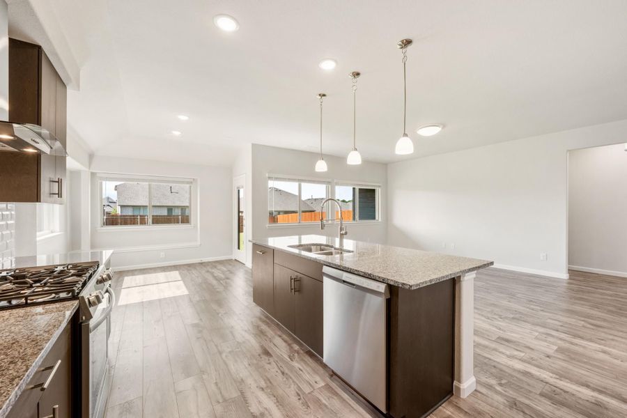 Kitchen with dark cabinet island, granite countertops, stainless appliances, and pendant lights over hardwood floors