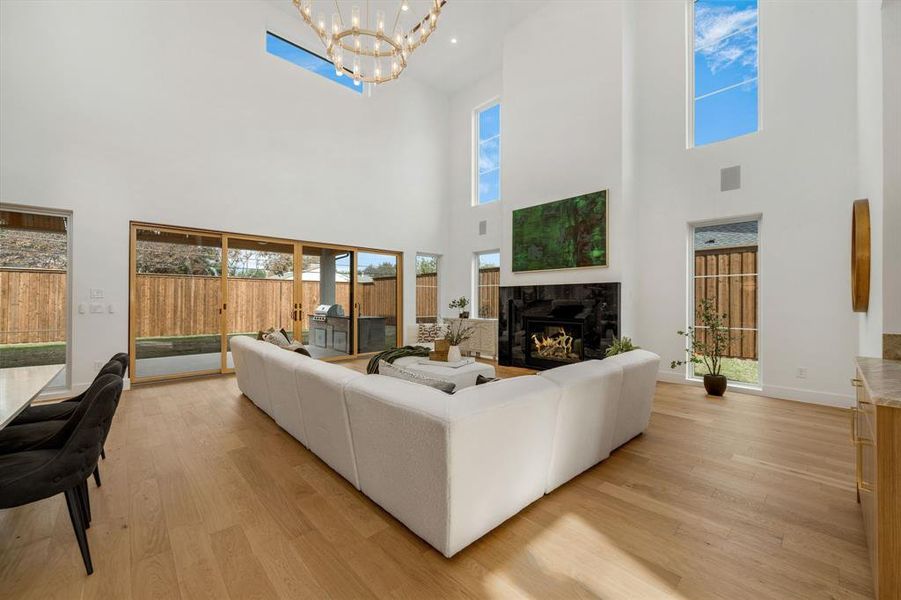 Living room featuring light wood-type flooring, a premium fireplace, a chandelier, and a high ceiling Living room featuring light wood-type flooring, a premium fireplace, a chandelier, and a high ceiling