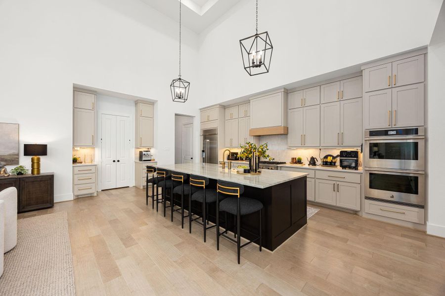This kitchen features an elegant design with high ceilings, modern pendant lighting, and a large island with seating. It includes ample cabinetry, stainless steel appliances, and a bright, open layout ideal for cooking and entertaining.