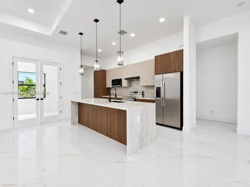 Kitchen featuring a waterfall island with a stone-finish countertop, two-tone cabinetry, stainless steel appliances, pendant lighting, and polished stone-finish flooring