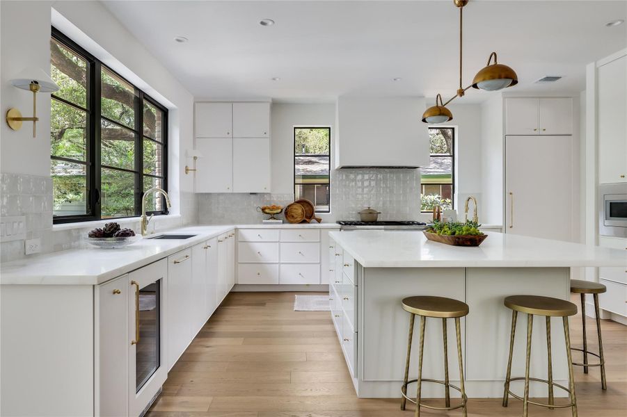 Open-concept kitchen featuring an expansive island with seating, white cabinetry, integrated appliances, wood-finish flooring, and black-framed windows