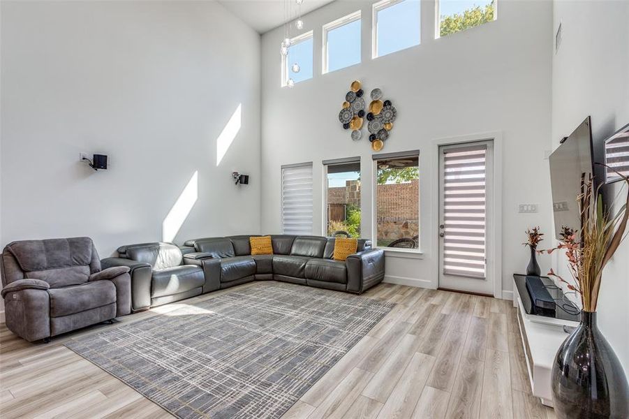 Expansive living room with soaring ceilings and an abundance of windows adorned with luxury motorized blinds. Gorgeous, easy-to-clean light wood–style luxury vinyl plank flooring flows seamlessly to the outdoor patio—perfect for indoor-outdoor living and entertaining! Expansive living room with soaring ceilings and an abundance of windows adorned with luxury motorized blinds. Gorgeous, easy-to-clean light wood–style luxury vinyl plank flooring flows seamlessly to the outdoor patio—perfect for indoor-outdoor living and entertaining!