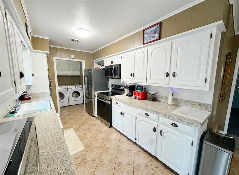 Kitchen featuring crown molding, washing machine and clothes dryer, white cabinets, appliances with stainless steel finishes, and light stone countertops