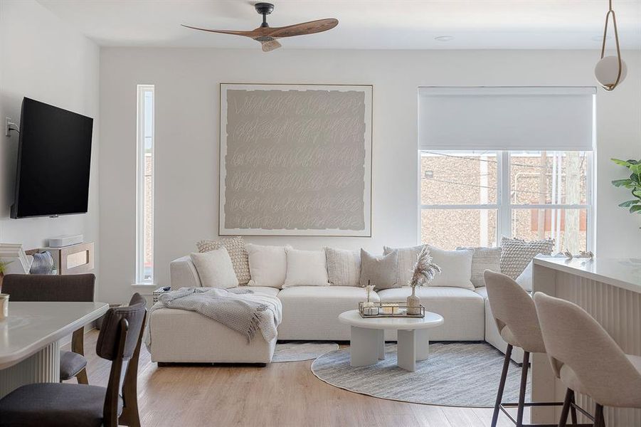 Bright living area with recessed lighting, wood-finish flooring, a contemporary ceiling fan, and large windows with roller shades