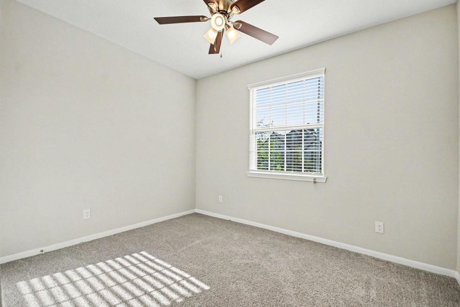 2nd bedroom with soft carpet flooring, a ceiling fan for comfort, and natural light streaming through a large window.