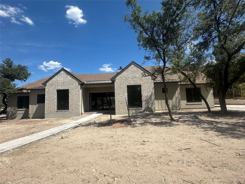 Mature trees frame the stone-accented facade of this single-level home with a concrete walkway.