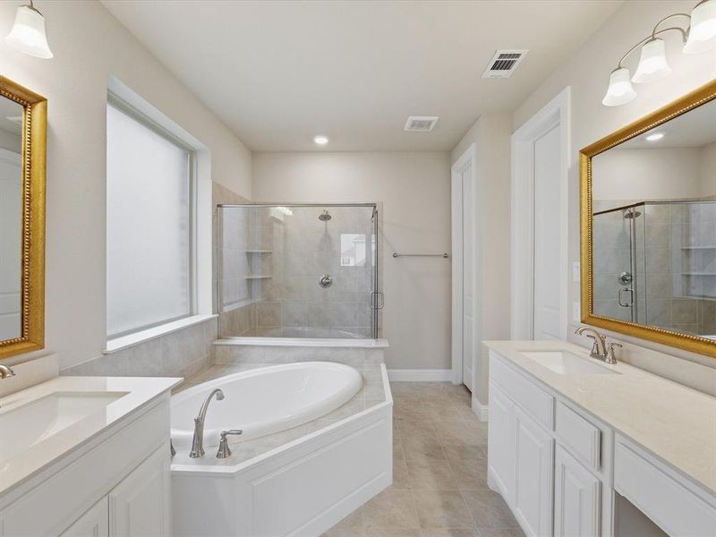 Spacious bathroom featuring a built-in soaking tub, a walk-in shower with glass enclosure, dual vanity sinks with white cabinetry, and large framed mirrors