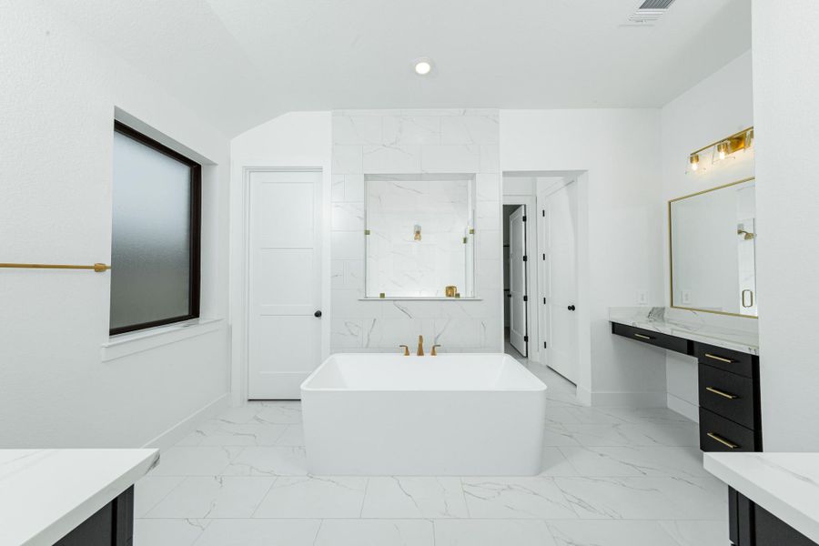 The centerpiece of this contemporary primary bath is the deep, freestanding bathtub with gorgeous marble tile, offering an ideal spot for relaxation with a unique view into the walk-in shower.