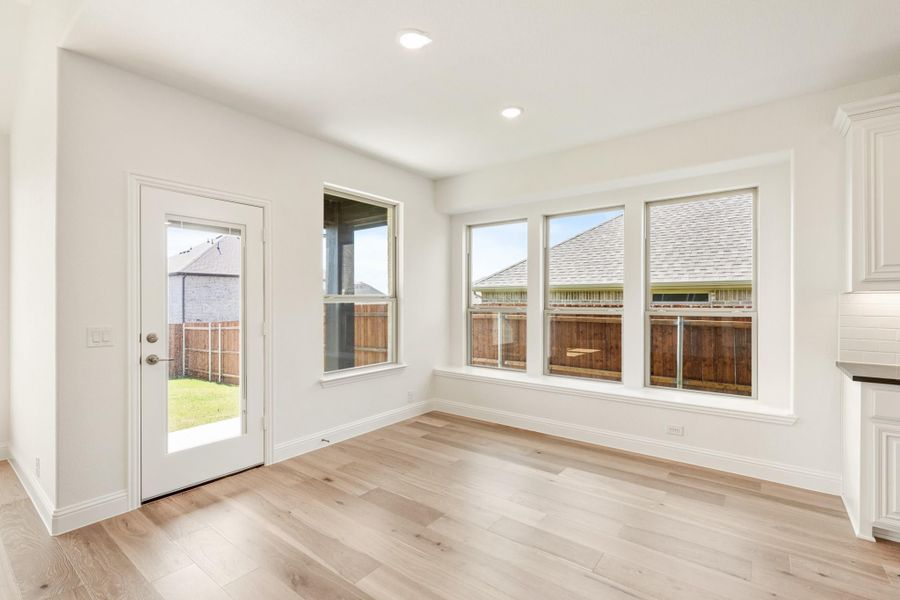 Bright breakfast nook with light wood floors, three windows, and glass back door overlooking fenced yard Bright breakfast nook with light wood floors, three windows, and glass back door overlooking fenced yard