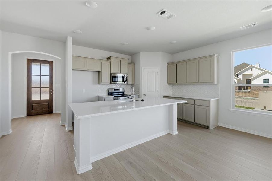 Kitchen featuring stainless steel appliances, arched walkways, light stone countertops, a kitchen island with sink, and light wood finished floors