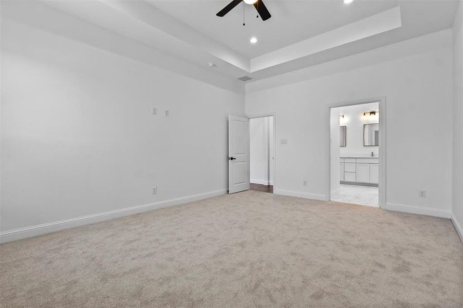 Unfurnished bedroom with a raised ceiling, light carpet, ensuite bath, recessed lighting, and a ceiling fan Unfurnished bedroom with a raised ceiling, light carpet, ensuite bath, recessed lighting, and a ceiling fan