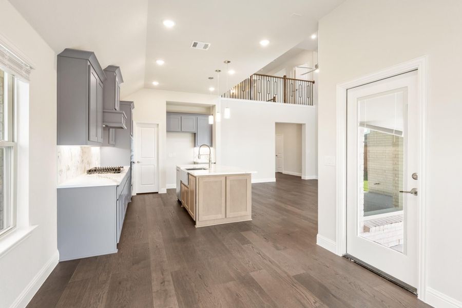 Open kitchen with gray cabinets, center island, dark hardwood floors, and second-floor balcony visible above Open kitchen with gray cabinets, center island, dark hardwood floors, and second-floor balcony visible above