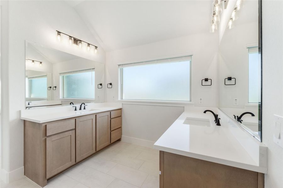 Bathroom with dual vanities, white quartz countertops, wood cabinets, and large mirrors with modern lighting