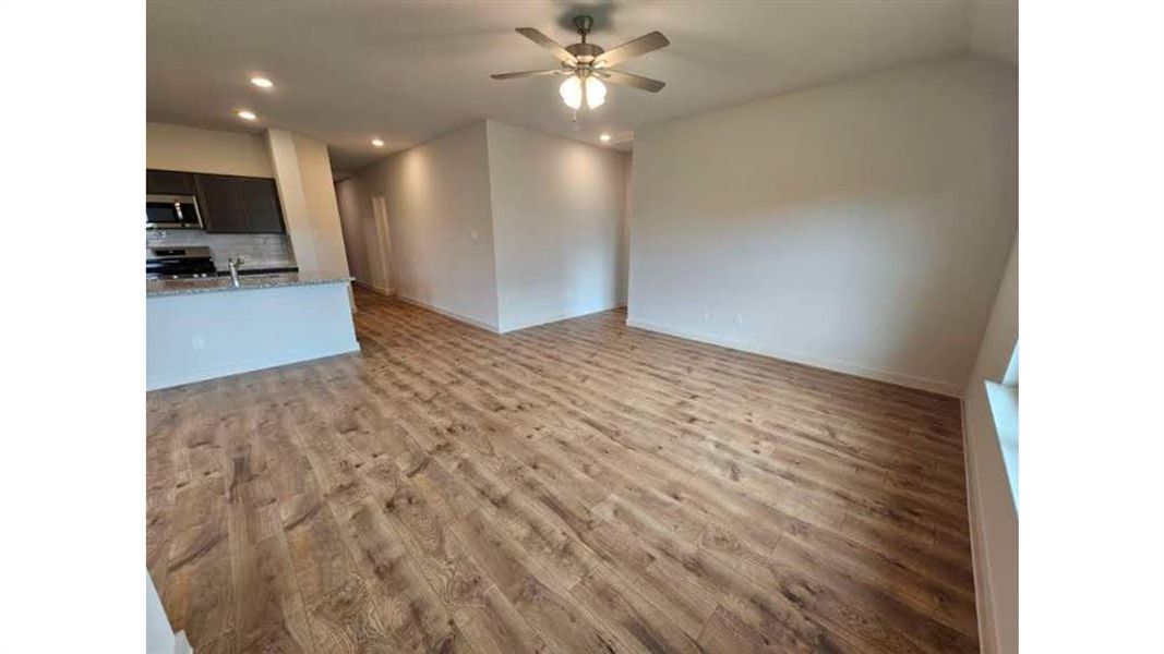 Open-concept living area featuring wood-finish flooring, a ceiling fan, recessed lighting, and a partial view of the kitchen with dark cabinetry and stainless steel appliances