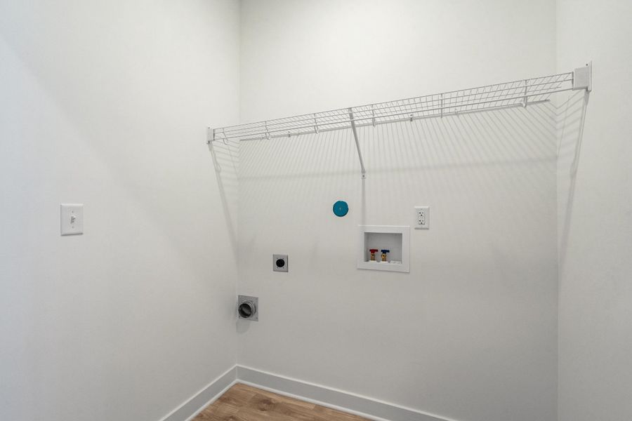 Dedicated laundry area featuring a wire storage shelf, utility hookups, and wood-finish flooring