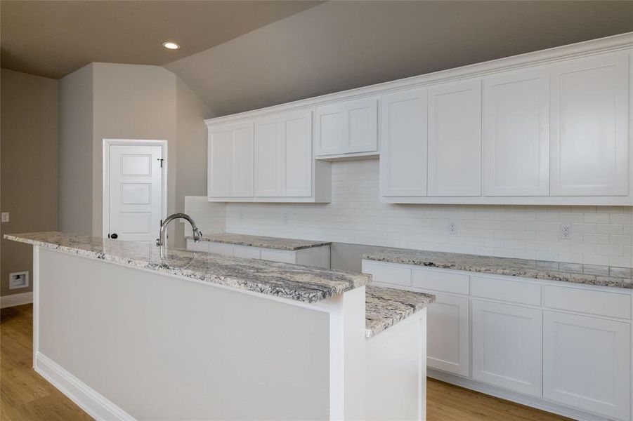 Kitchen with white cabinetry, light wood-type flooring, tasteful backsplash, and an island with sink