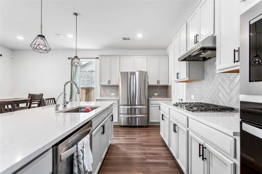 Kitchen featuring stainless steel appliances, under cabinet range hood, recessed lighting, backsplash, and hanging light fixtures