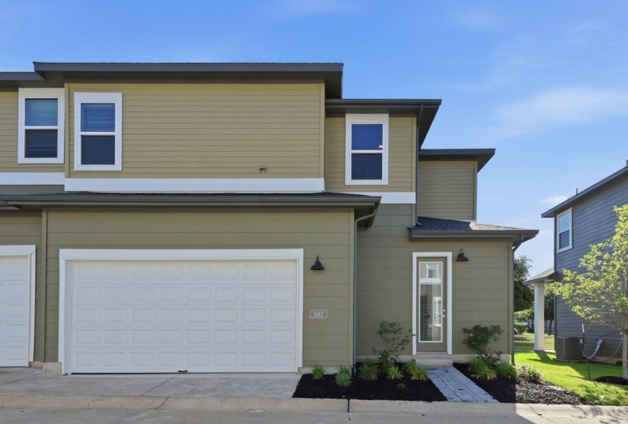 Two-story exterior with a two-tone facade, featuring a prominent white garage door, multiple windows with white trim, and a covered entry with an adjacent light fixture Two-story exterior with a two-tone facade, featuring a prominent white garage door, multiple windows with white trim, and a covered entry with an adjacent light fixture