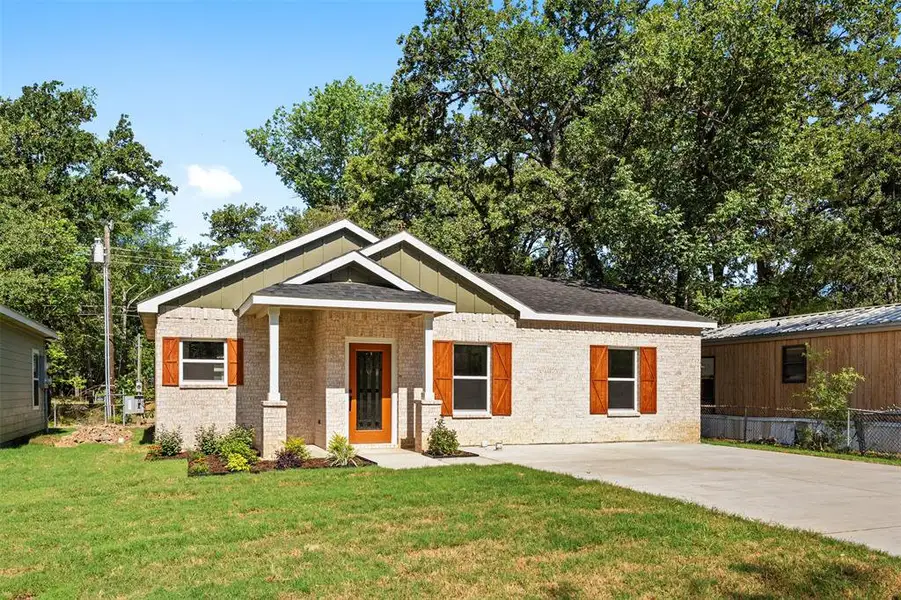 Brick facade residence with a covered entry, wood-finish front door, and decorative window shutters Brick facade residence with a covered entry, wood-finish front door, and decorative window shutters