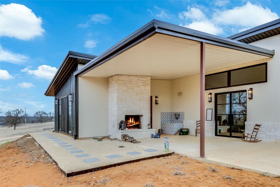 Rear view of property with an outdoor stone fireplace, stone siding, and a patio area