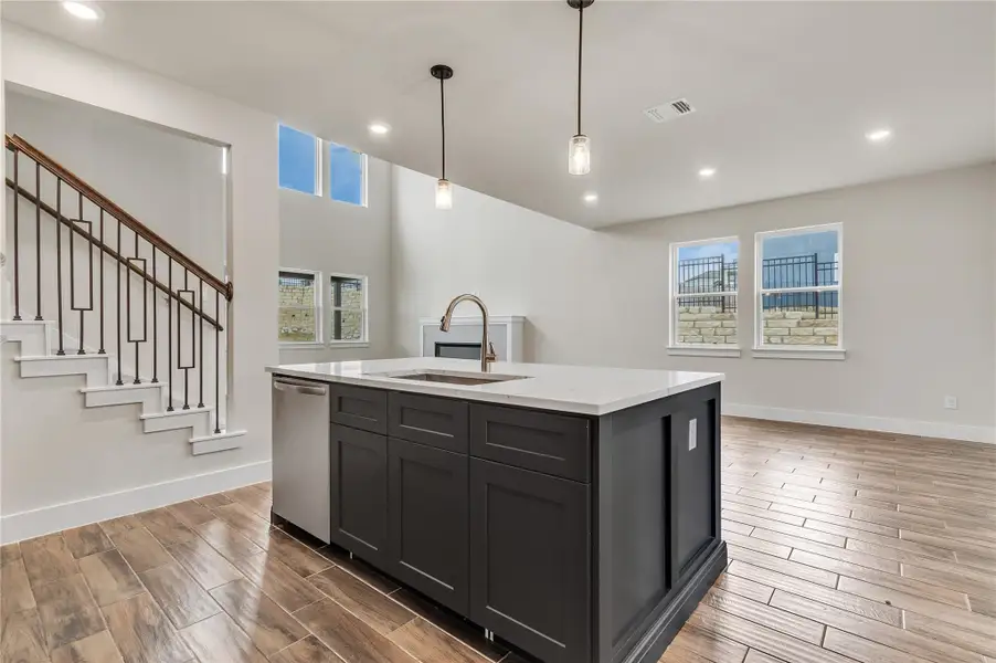 Modern kitchen island with sleek finishes anchors an open-concept living space, featuring a grand staircase.