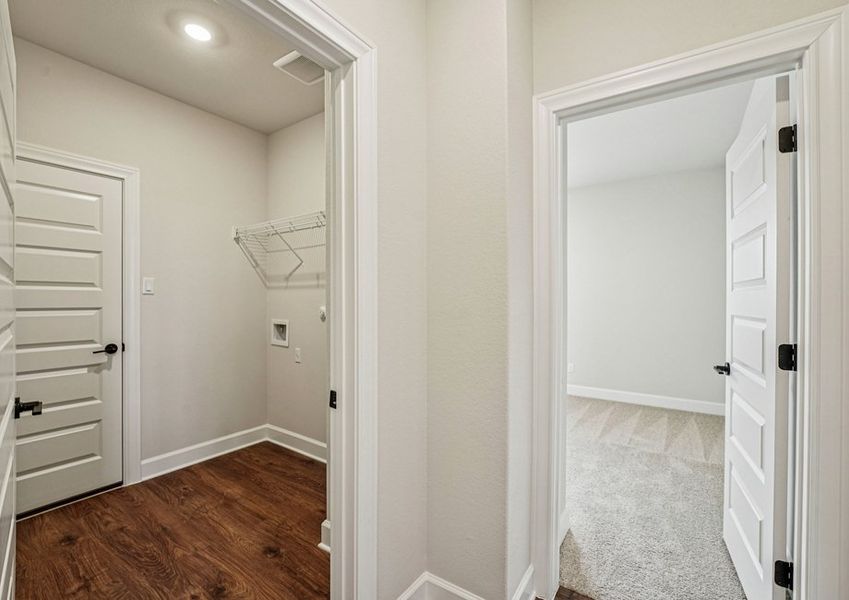 Laundry room featuring built-in wire shelving and a doorway to the master bath. Laundry room featuring built-in wire shelving and a doorway to the master bath.