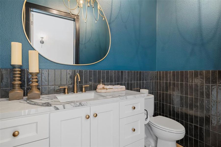 Bathroom featuring a textured wall, tile walls, vanity, and wainscoting