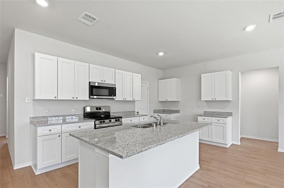 Modern kitchen featuring a central island, white shaker cabinetry, stainless steel appliances, recessed lighting, and wood-finish flooring Modern kitchen featuring a central island, white shaker cabinetry, stainless steel appliances, recessed lighting, and wood-finish flooring