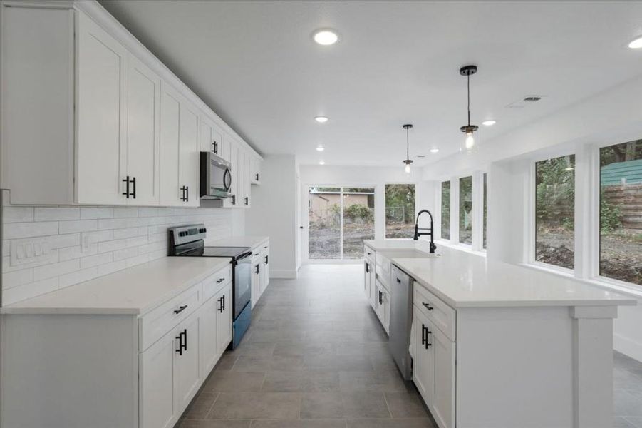 Kitchen with decorative light fixtures, stainless steel appliances, sink, and a center island with sink