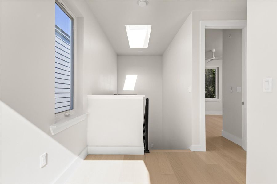 Natural light pours through dual overhead skylights illuminating this modern upper hallway and staircase.