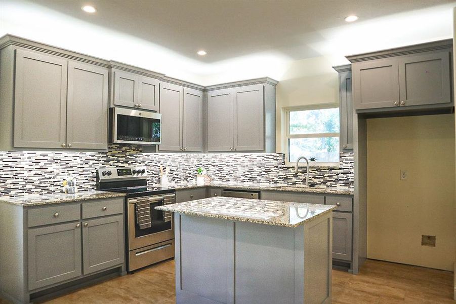 Kitchen with a kitchen island, appliances with stainless steel finishes, light stone countertops, gray cabinets, and sink