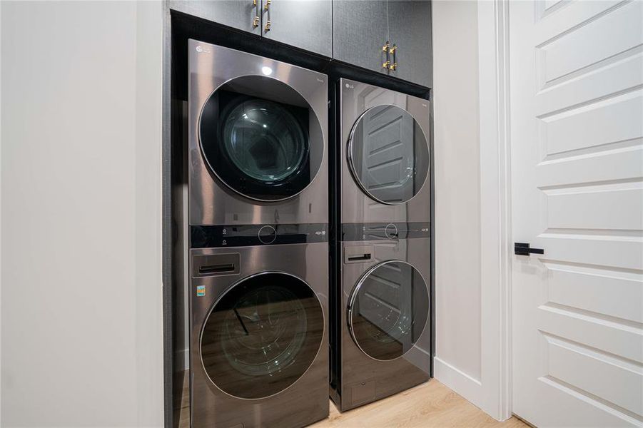 Laundry room with cabinet space, stacked washer / drying machine, and light wood finished floors Laundry room with cabinet space, stacked washer / drying machine, and light wood finished floors