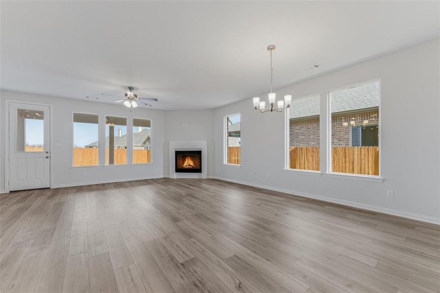 Unfurnished living room featuring a warm lit fireplace, light wood-style floors, a ceiling fan, and a chandelier