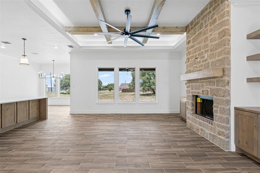 Unfurnished living room with plenty of natural light, beam ceiling, a chandelier, a stone fireplace, and wood finished floors Unfurnished living room with plenty of natural light, beam ceiling, a chandelier, a stone fireplace, and wood finished floors