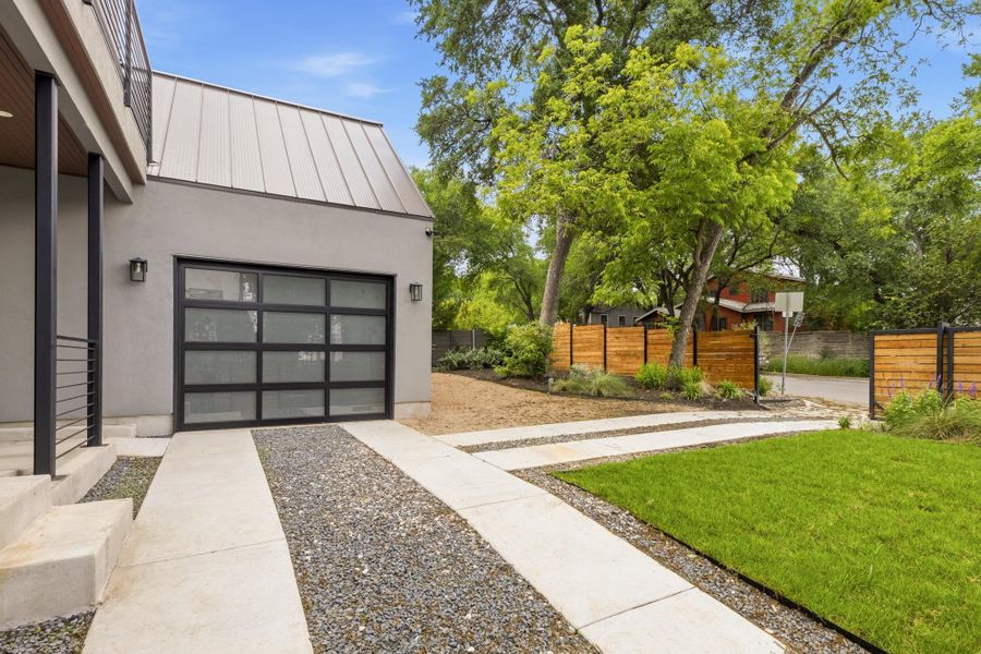 Modern exterior featuring a glass panel garage door, corrugated metal roof, and sleek exterior lighting