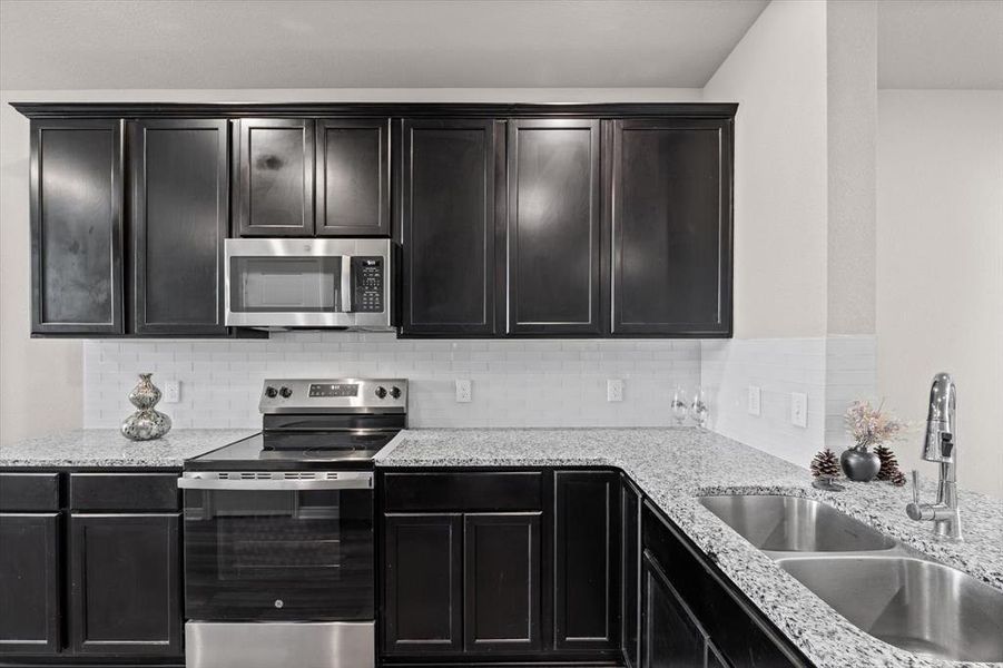 Kitchen featuring appliances with stainless steel finishes, light stone countertops, decorative backsplash, and dark cabinetry Kitchen featuring appliances with stainless steel finishes, light stone countertops, decorative backsplash, and dark cabinetry