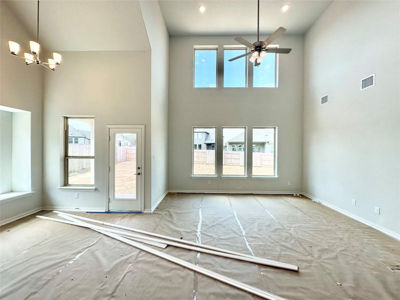 Unfurnished living room featuring a high ceiling, a chandelier, and ceiling fan Unfurnished living room featuring a high ceiling, a chandelier, and ceiling fan