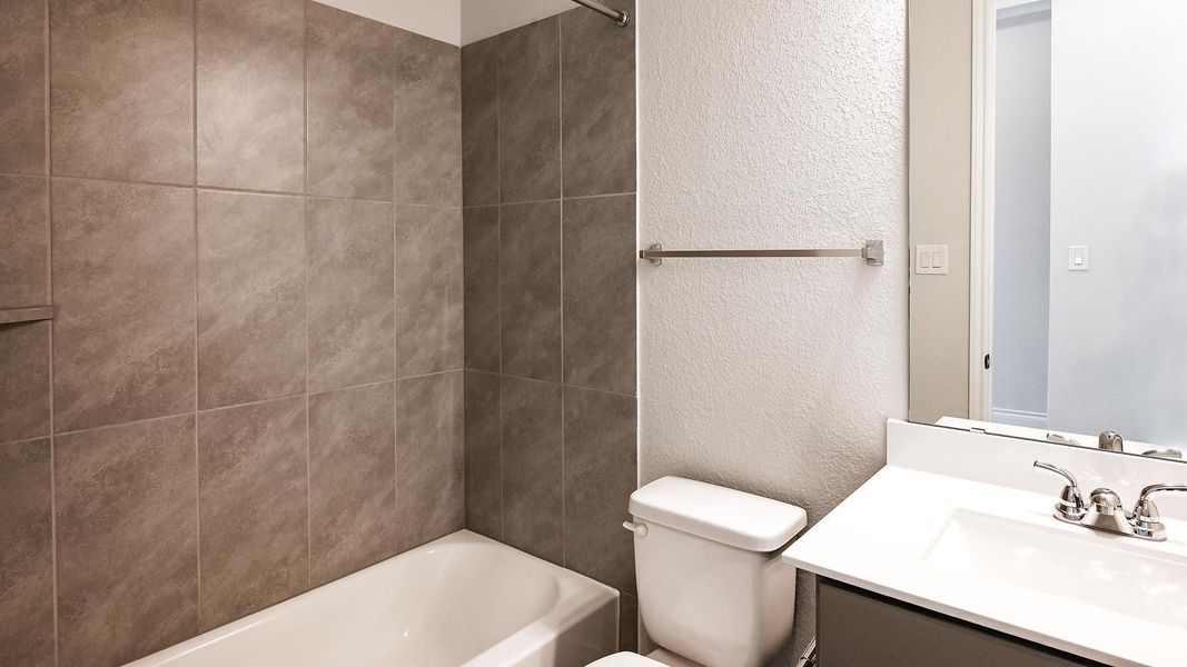 Bathroom featuring a textured wall, toilet, vanity, and washtub / shower combination Bathroom featuring a textured wall, toilet, vanity, and washtub / shower combination