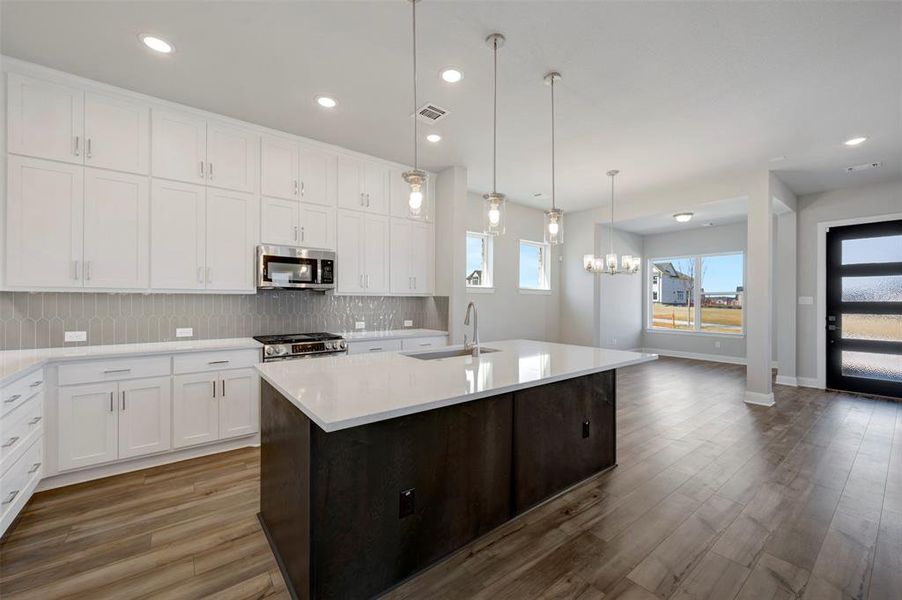 Kitchen featuring an island with sink, stainless steel appliances, dual tone cabinetry, dark wood-style floors, and backsplash