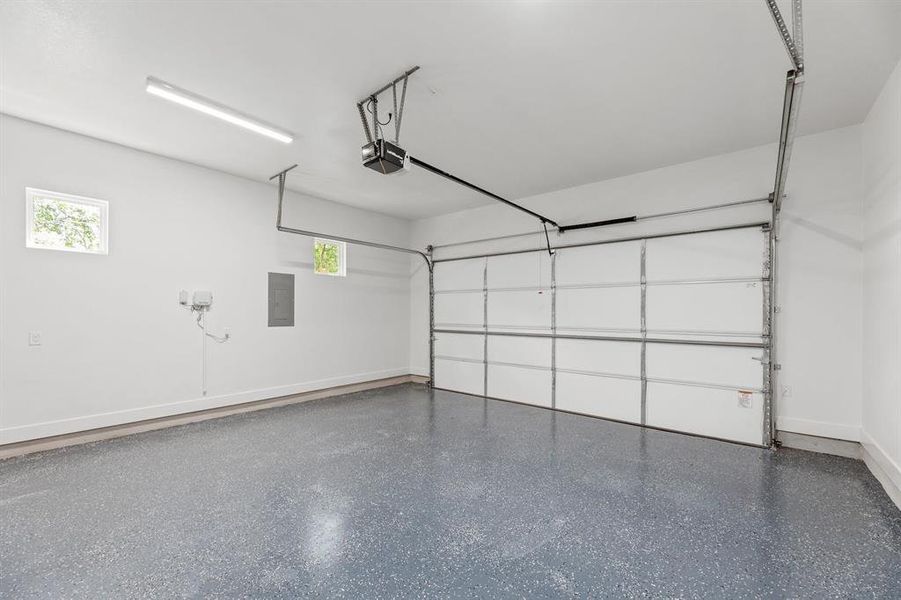 Garage featuring electric panel, a garage door opener, and baseboards