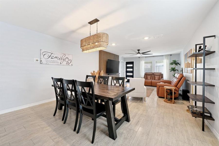 Dining area featuring a rectangular wood-finish table with seating for six, illuminated by a multi-tiered woven pendant light