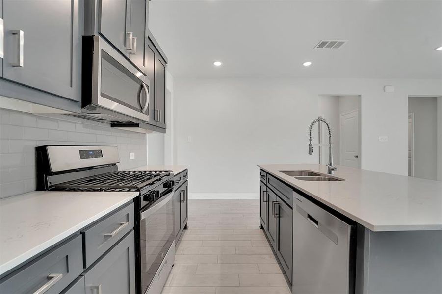 Kitchen with tasteful backsplash, visible vents, appliances with stainless steel finishes, gray cabinetry, and a sink Kitchen with tasteful backsplash, visible vents, appliances with stainless steel finishes, gray cabinetry, and a sink
