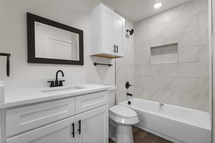 Bathroom featuring a white vanity with black hardware, a black framed mirror, a white bathtub with light-colored tile surround, and a built-in shower niche