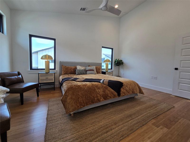 Bedroom featuring baseboards, wood finished floors, visible vents, and high vaulted ceiling Bedroom featuring baseboards, wood finished floors, visible vents, and high vaulted ceiling