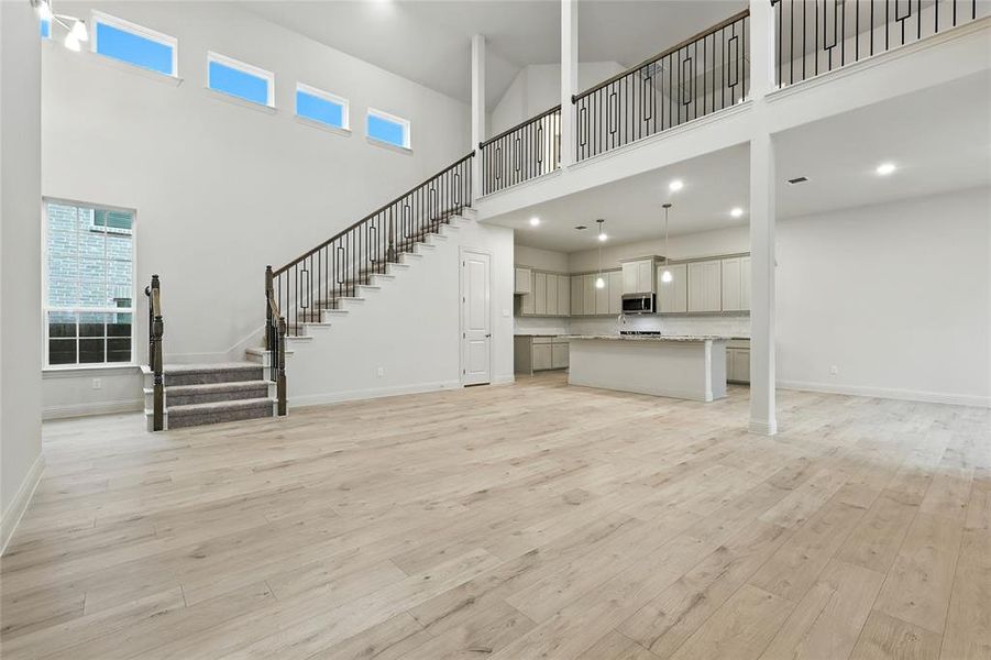 Unfurnished living room with a high ceiling, stairway, light wood-style flooring, and recessed lighting
